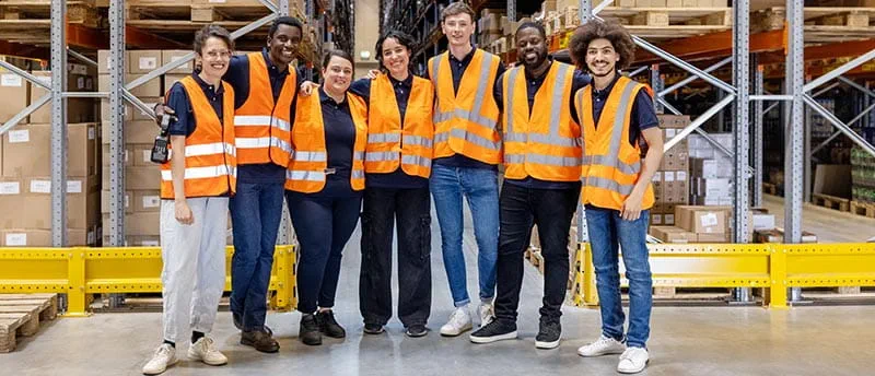 Gruppe von Arbeitern in einer Lagerhalle mit Warnwesten - DIS AG Gruppe von Arbeitern in einer Lagerhalle mit Warnwesten - DIS AG